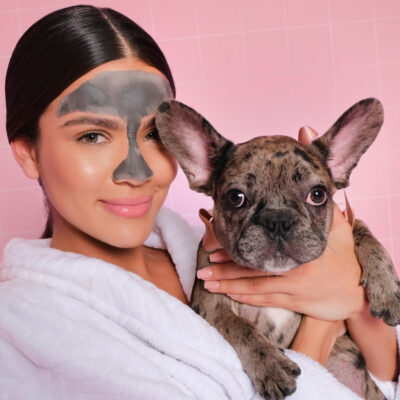 modelo mujer latina sonriente con mascarilla de barro de infinitek paris aplicada en el rostro o cara, sosteniendo su mascota o perro